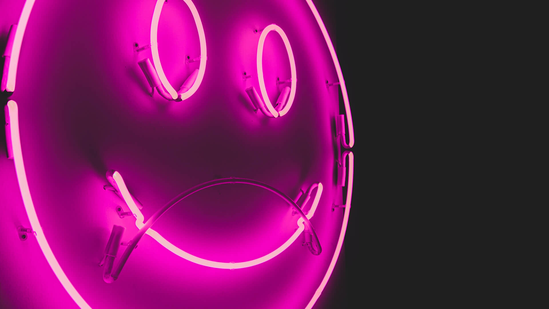 Purple neon sign of a smiley face in a black background.