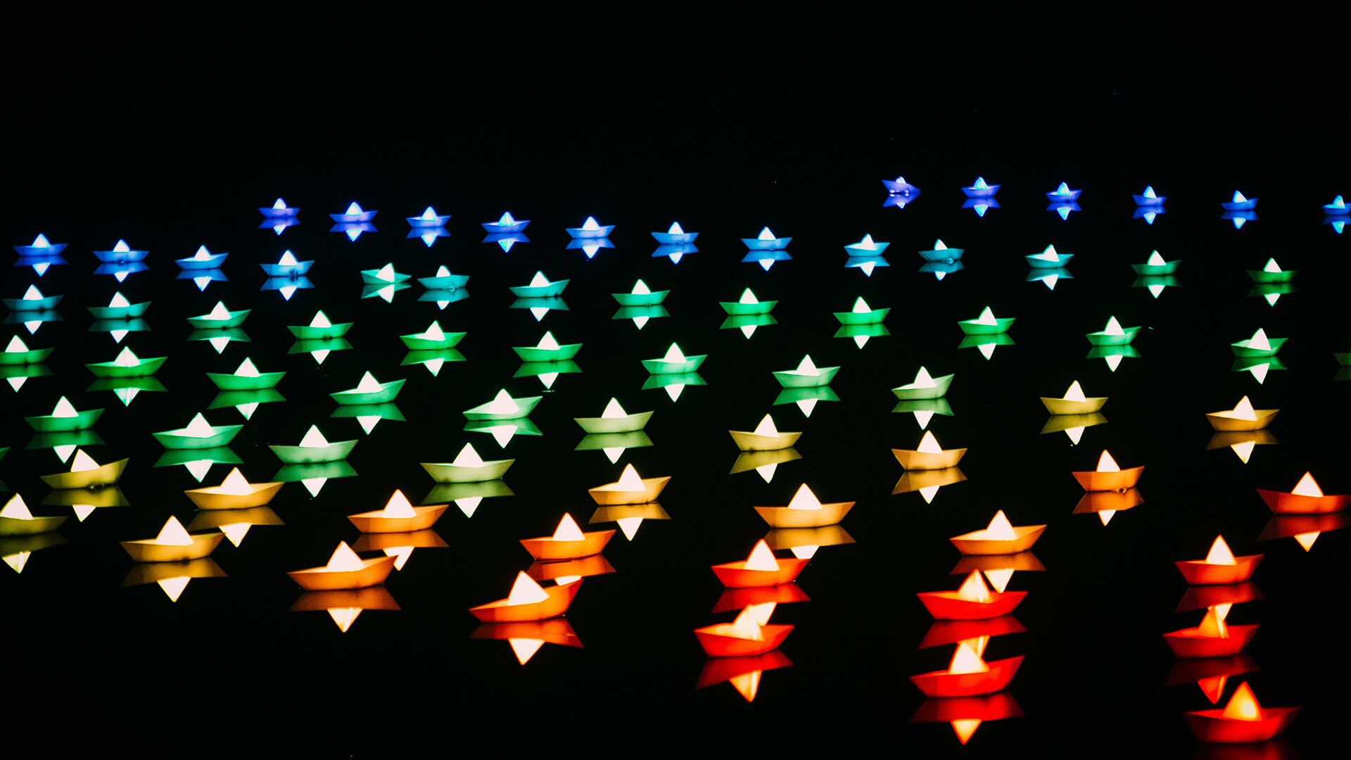 Blue, red, yellow and green paper boats in dark water. 