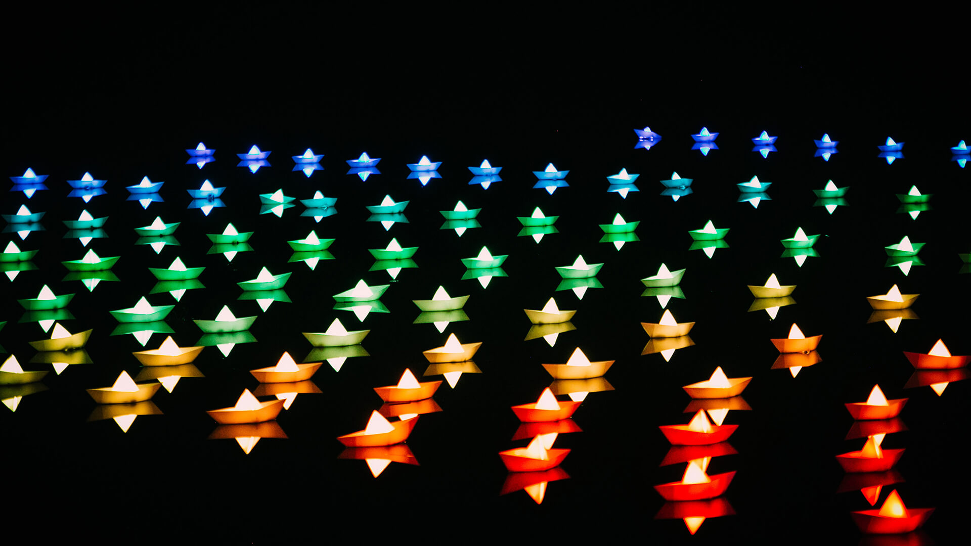 Blue, red, yellow and green paper boats in dark water.