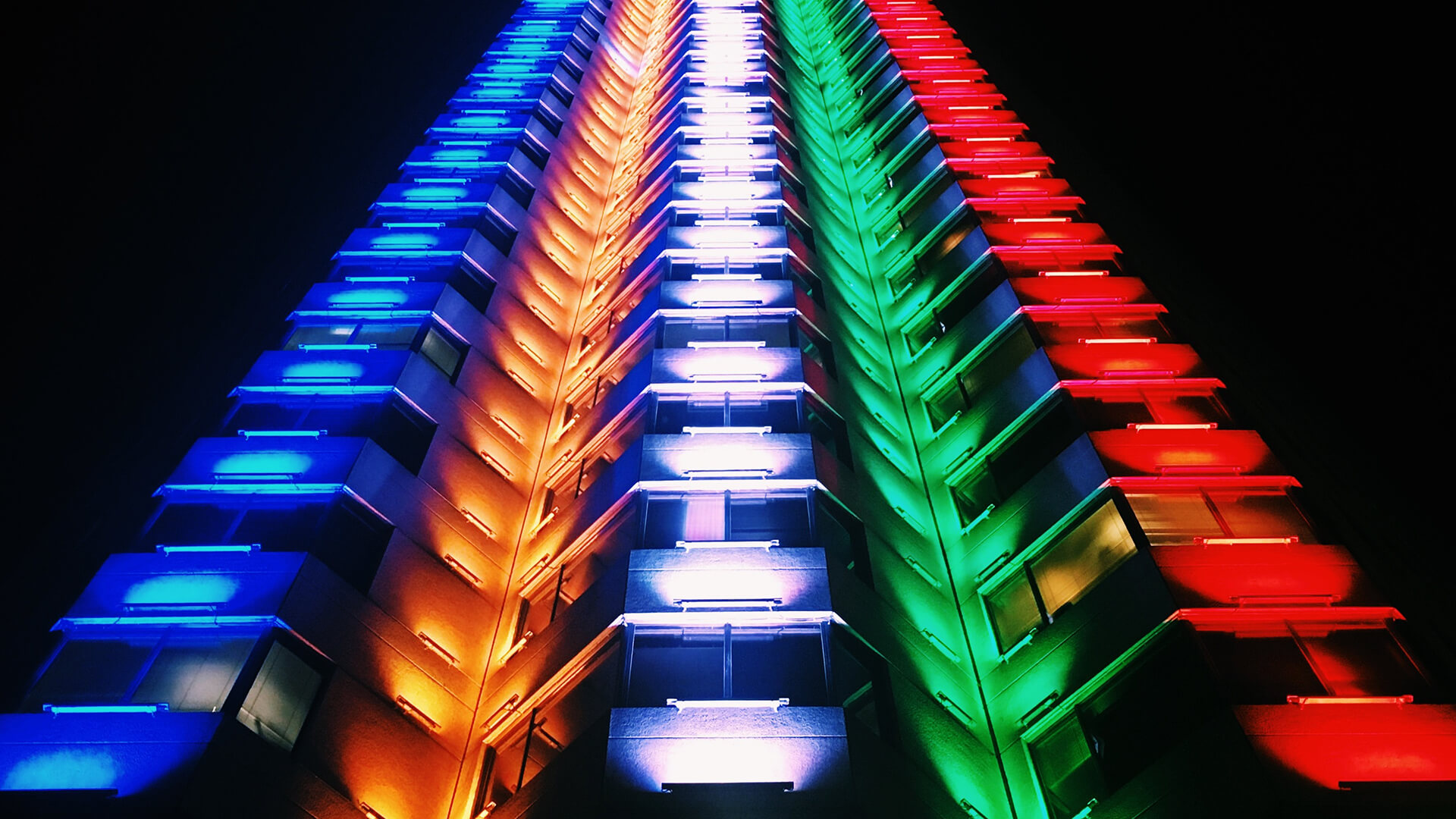 Exterior of an apartment building at night, with red, green, blue and yellow light shining on it 